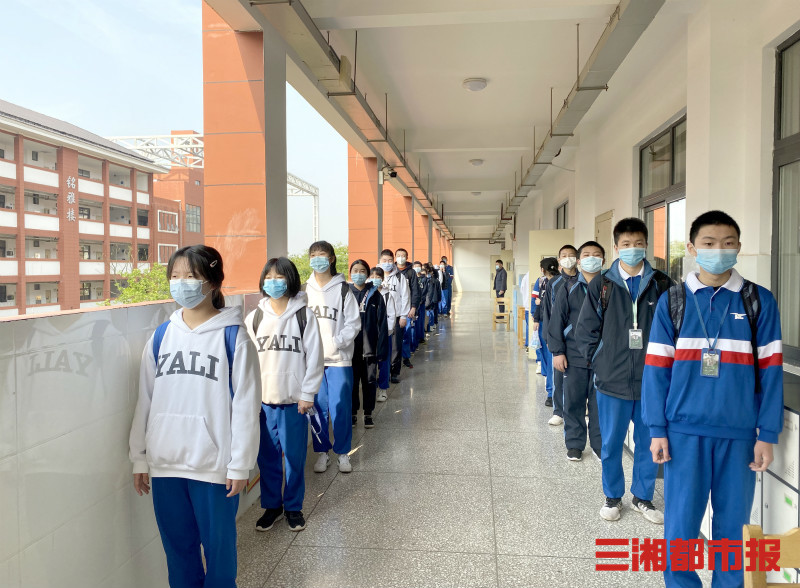 (学生按1米间距有序排队,通过额温枪监测体温进入教室)