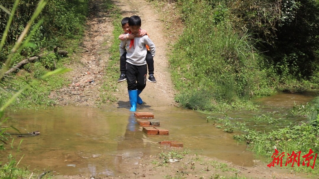 上学的时候,易庆红会穿上雨鞋背着弟弟走过门前的小河,然后牵着
